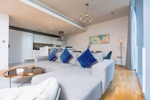 A modern living room with a sofa, a coffee table, and a dining area in the background.