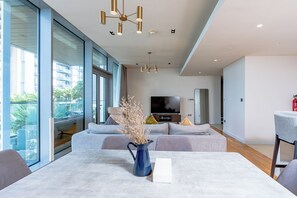 A modern living room with a large window, a sofa set, a television, and a vase with dried plants.