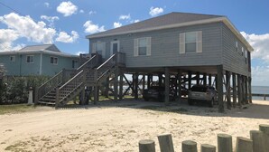 A two-story wooden house with a porch and a staircase leading to the upper level.