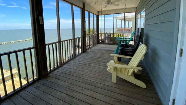 A covered porch with wooden railings, two ceiling fans, and a view of the ocean.