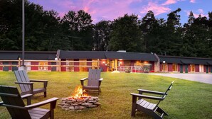 Eine Lodge mit Feuerstelle und Adirondack-Sesseln im Garten.