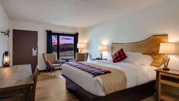 Ein Hotelzimmer mit einem großen Bett, einem Holztisch, einem Stuhl und Blick zum Himmel durch ein Fenster.