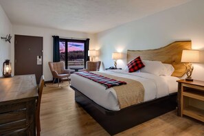 Une chambre d’hôtel avec un grand lit, un bureau en bois, une chaise et une vue sur le ciel par la fenêtre.