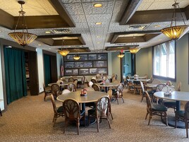 Um restaurante com mesas e cadeiras redondas, teto estampado e quadros nas paredes.