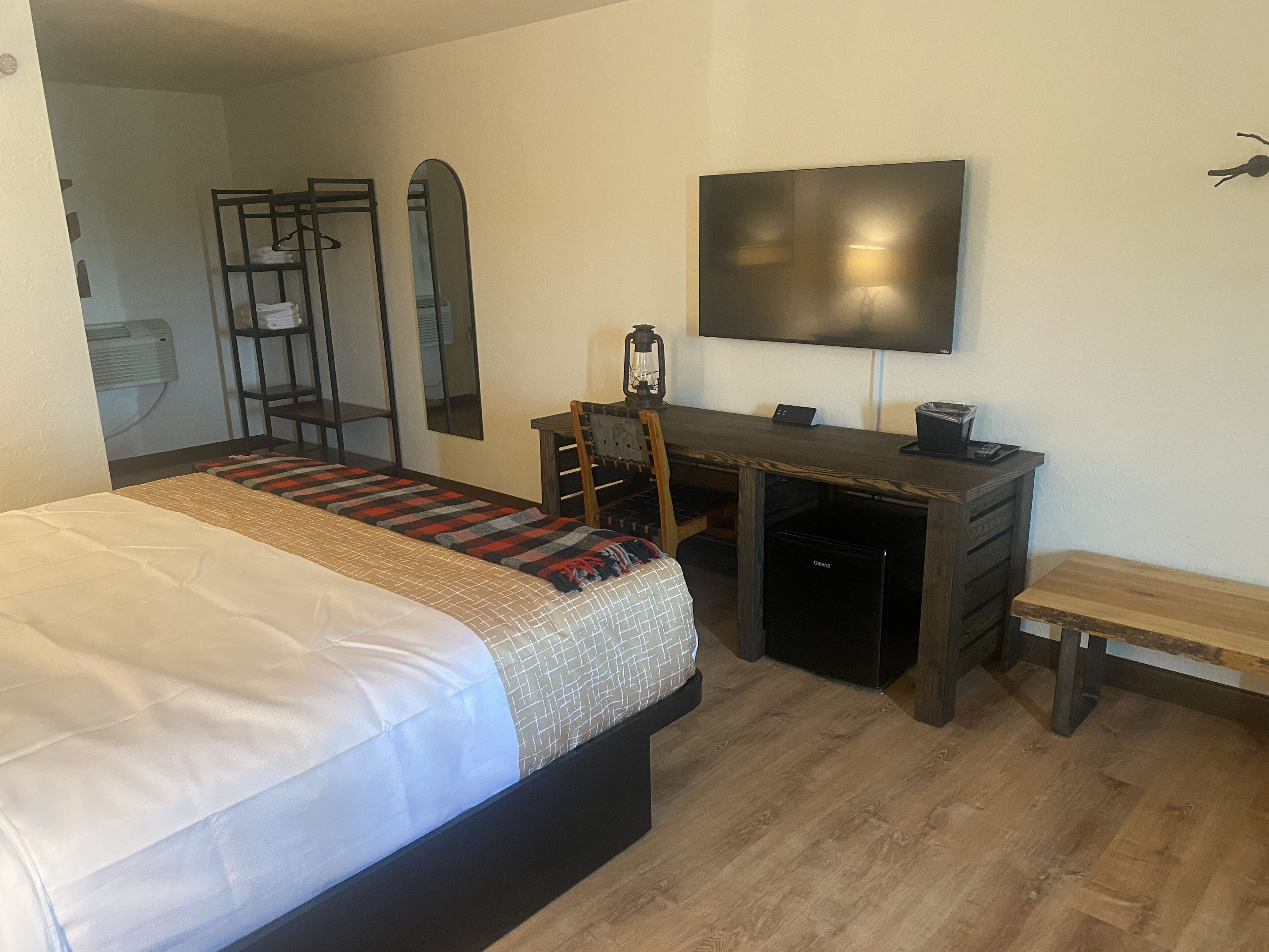 Een slaapkamer met een bed, een bureau, een stoel, een televisie en een bankje.