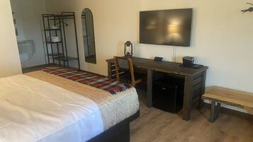 Een slaapkamer met een bed, een bureau, een stoel, een televisie en een bankje.