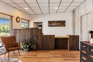 Zona de recepción con un mostrador de madera, un reloj, un cuadro y una planta en maceta.