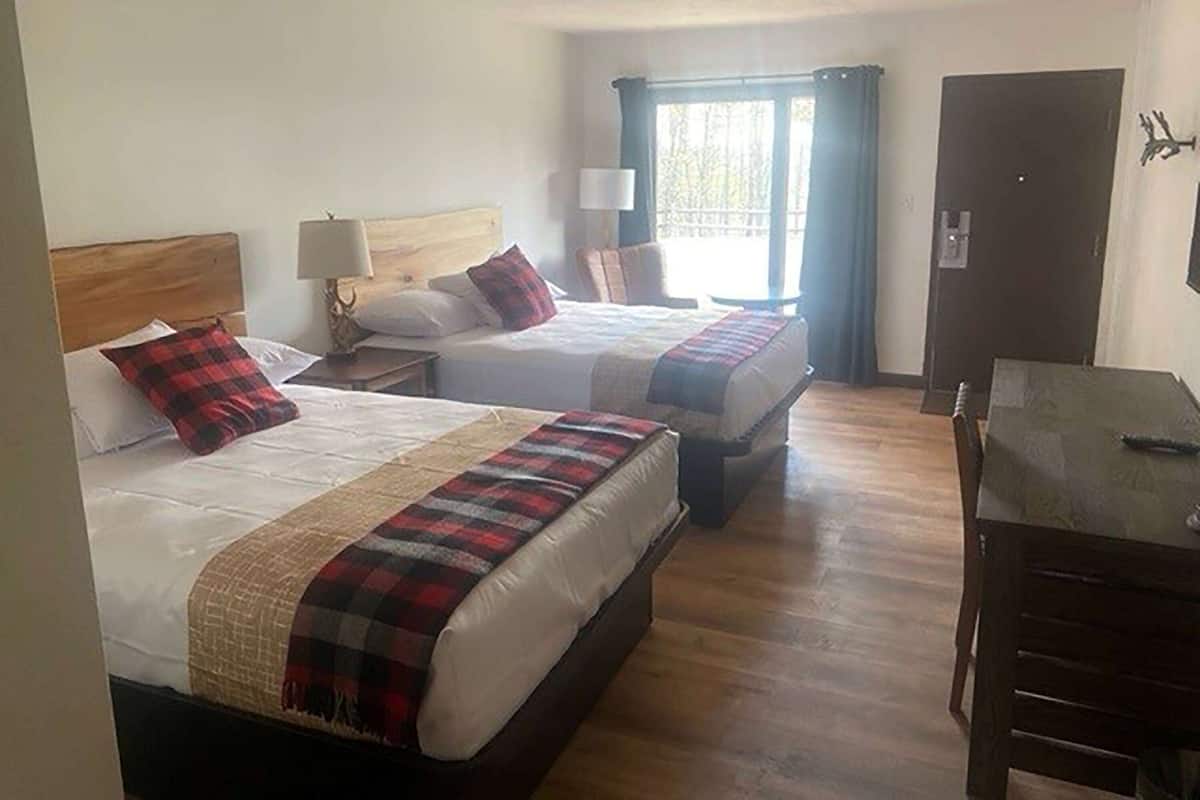 Une chambre d’hôtel avec deux lits, un plancher en bois, un bureau et une fenêtre avec des rideaux.