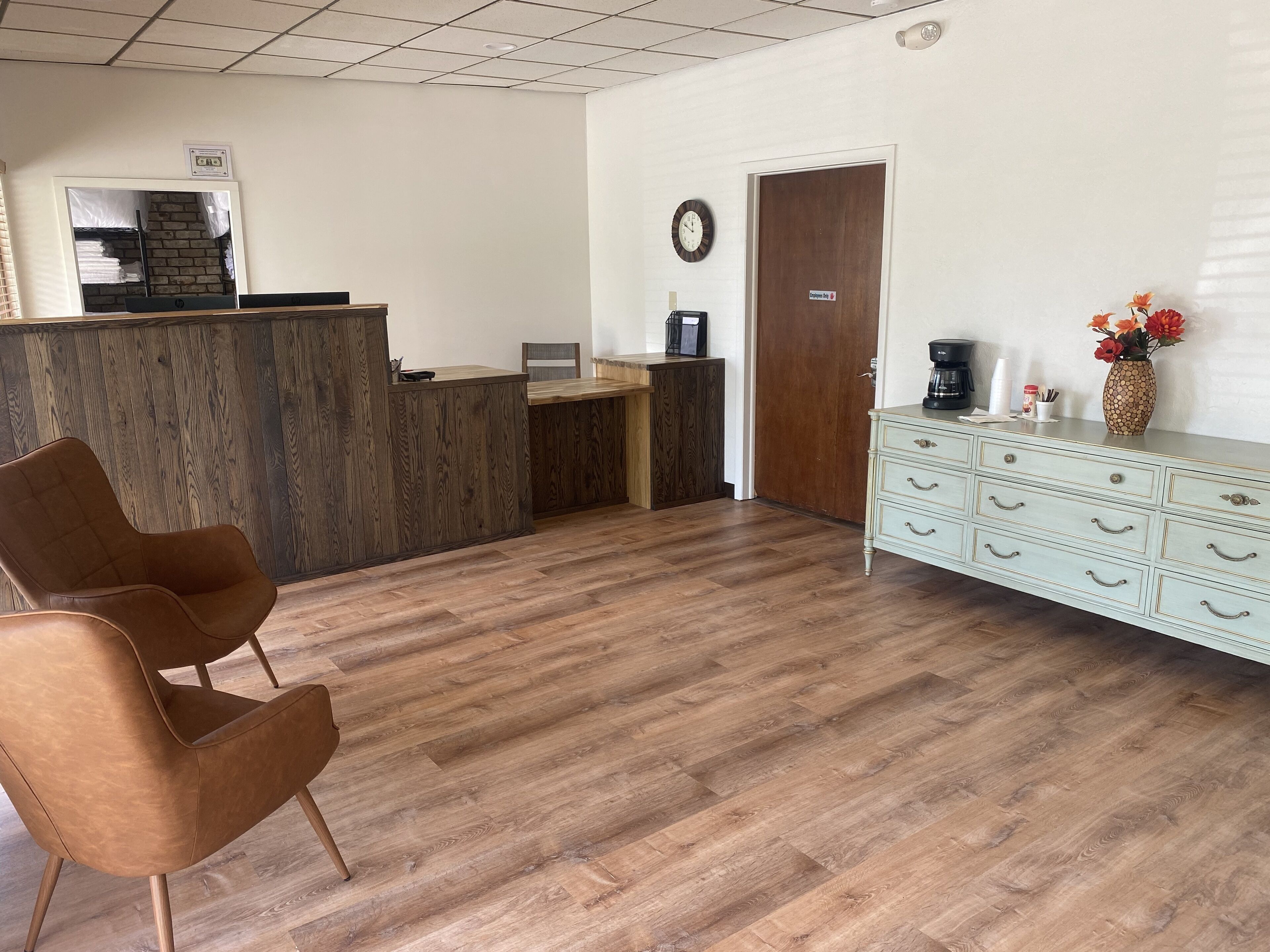 Una zona de recepción con un mostrador de madera, un reloj, una máquina de café y un jarrón con flores.
