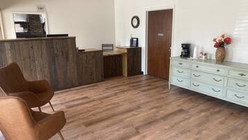 Una zona de recepción con un mostrador de madera, un reloj, una máquina de café y un jarrón con flores.