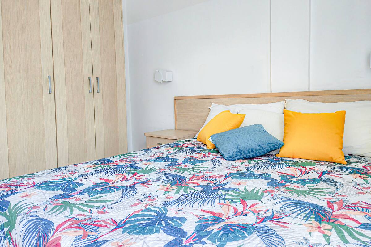 A bedroom with a bed, a wooden wardrobe, and a nightstand.