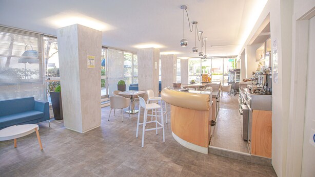 Eine moderne Küche mit einer gebogenen Kücheninsel, einem Essbereich mit blauem Sofa und weißen Stühlen sowie einer Bar mit einer Theke und Hockern.