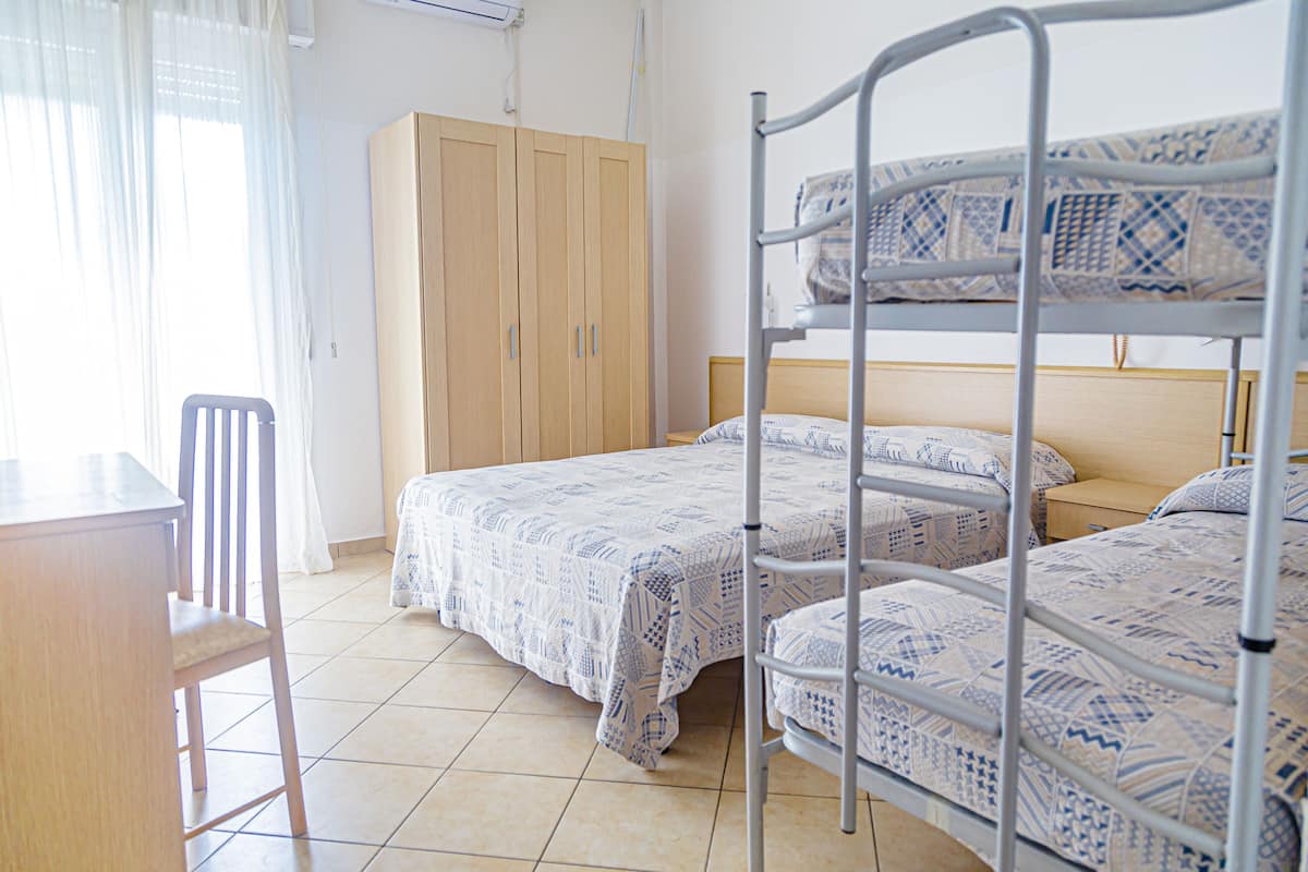 A dormitory room with bunk beds, a wooden wardrobe, a desk, and a chair.