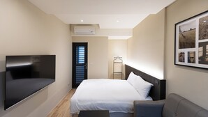 Une chambre d’hôtel moderne équipée d’un lit, d’un canapé, d’un téléviseur à écran plat, d’un porte-manteau et d’un tableau encadré au mur.