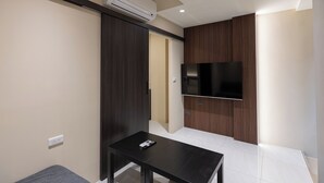 Une chambre d’hôtel moderne dotée d’un téléviseur à écran plat fixé à un mur en bois, d’une petite table avec une télécommande et d’une porte coulissante donnant sur une autre pièce.