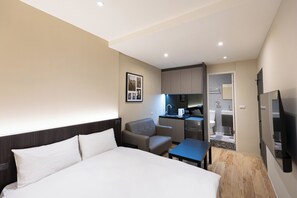 A hotel room with a bed, a desk, a chair, a TV, and a kitchenette.