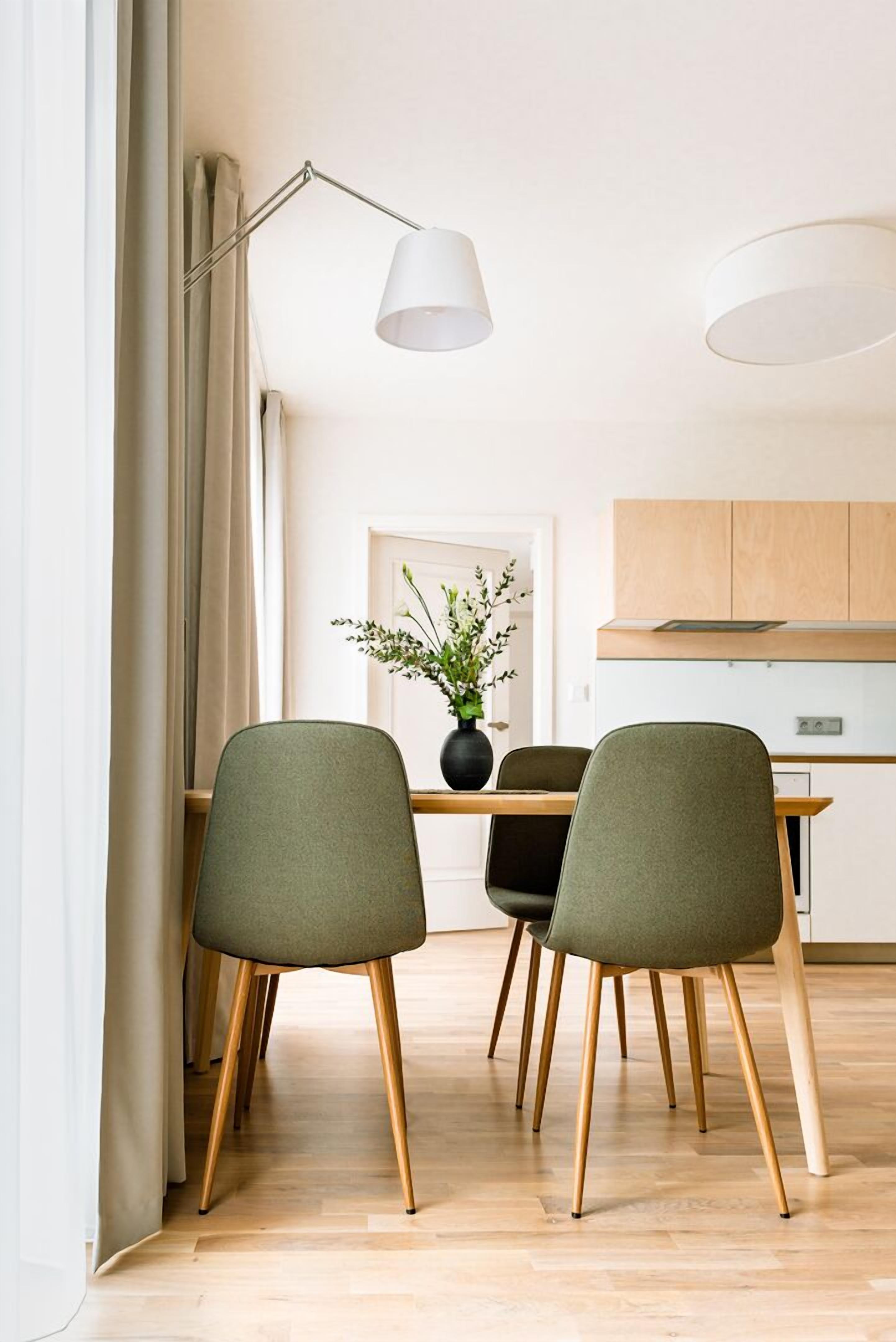 Ein zeitgemäßer Essbereich mit zwei grünen Stühlen, einem Holztisch und einer Stehlampe.