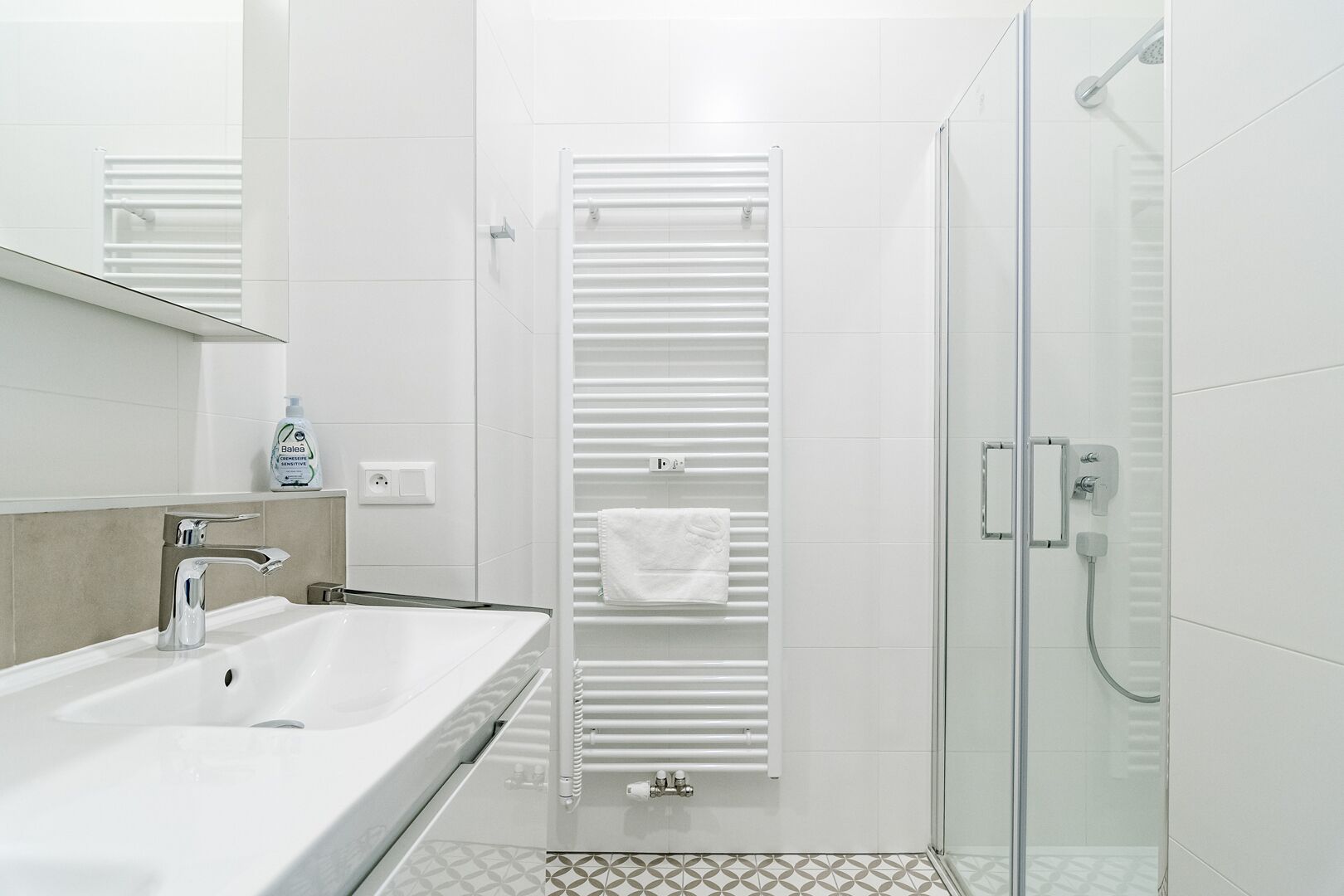 A modern bathroom with a white sink, a glass shower enclosure, and a towel rack with a white towel.