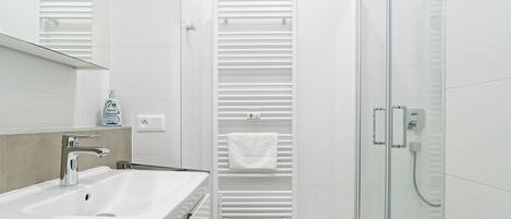 A modern bathroom with a white sink, a glass shower enclosure, and a towel rack with a white towel.