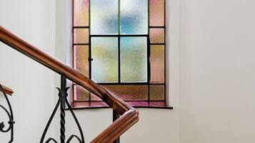 A staircase with a wooden handrail and black metal balusters, leading to a room with a large stained glass window.