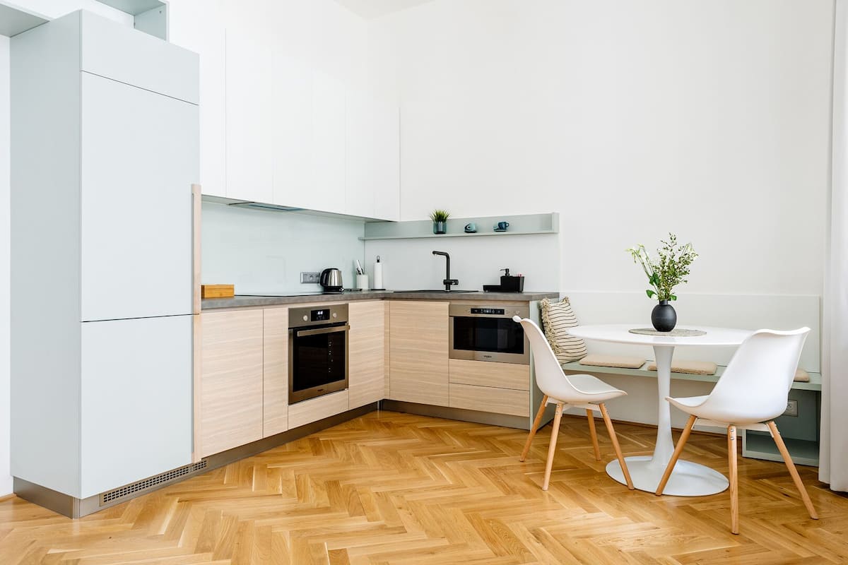 A modern kitchen with light wood cabinets, stainless steel appliances, and a herringbone wood floor.