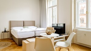 A hotel room with a bed, a TV, a desk, a chair, and large windows. - Apartment BRNO (Brno)