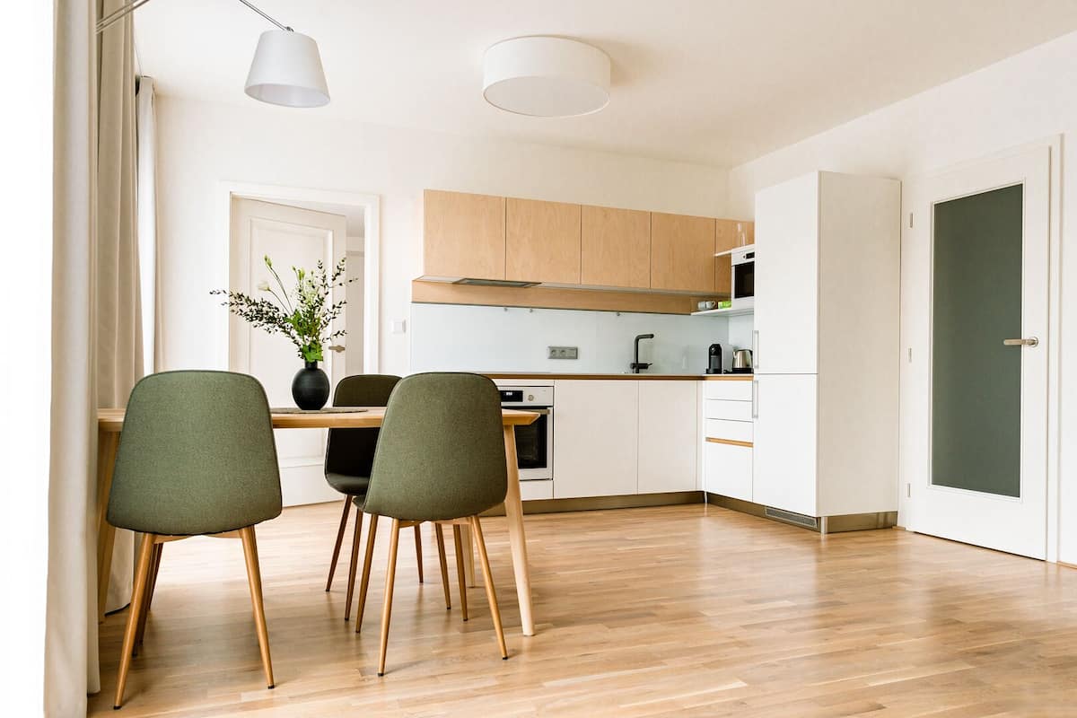 A modern kitchen with wooden cabinets, a dining area with two chairs, and a vase with flowers on the table.