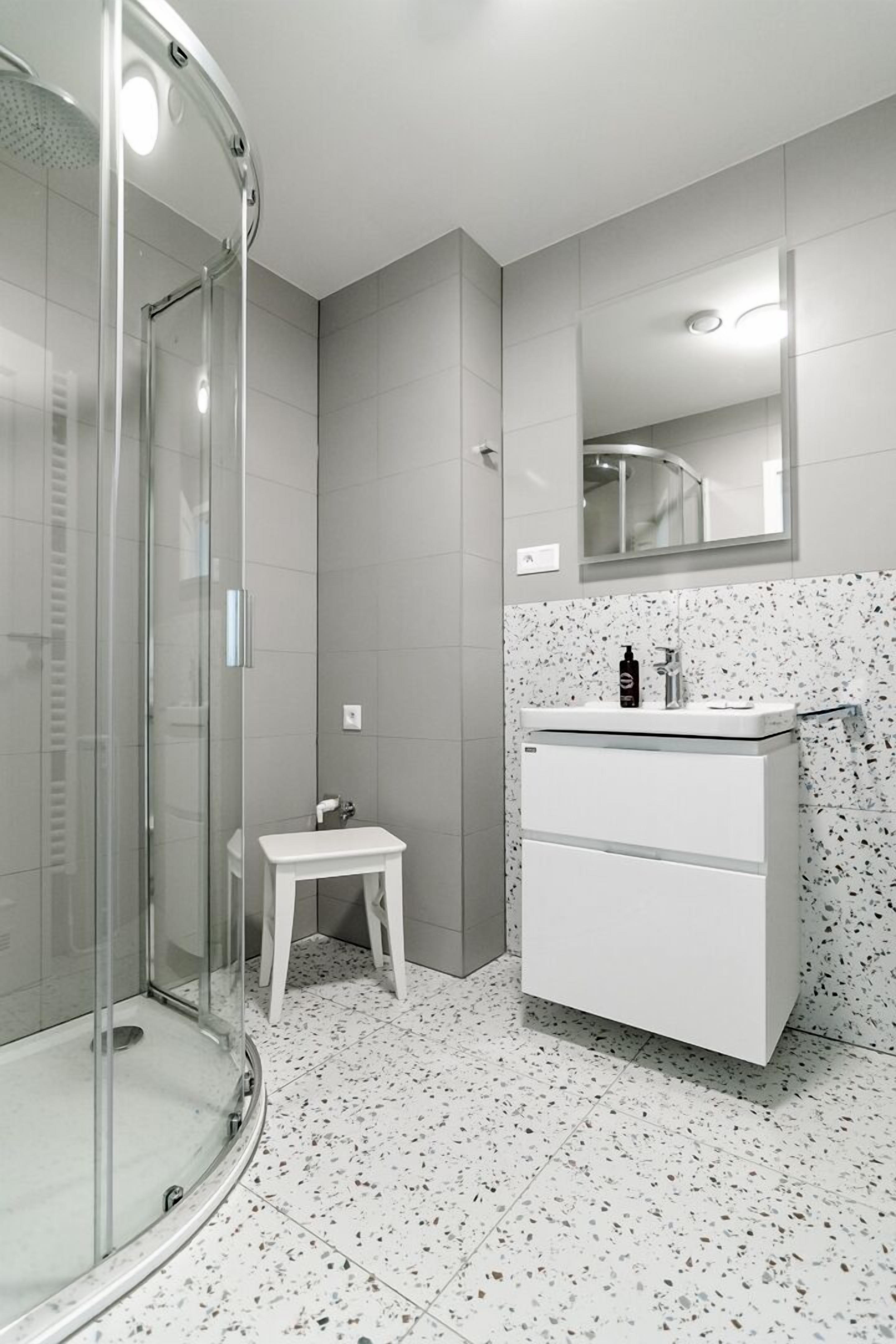 Une salle de bain moderne avec une douche à parois de verre, un petit meuble-lavabo blanc et un miroir au-dessus du lavabo.