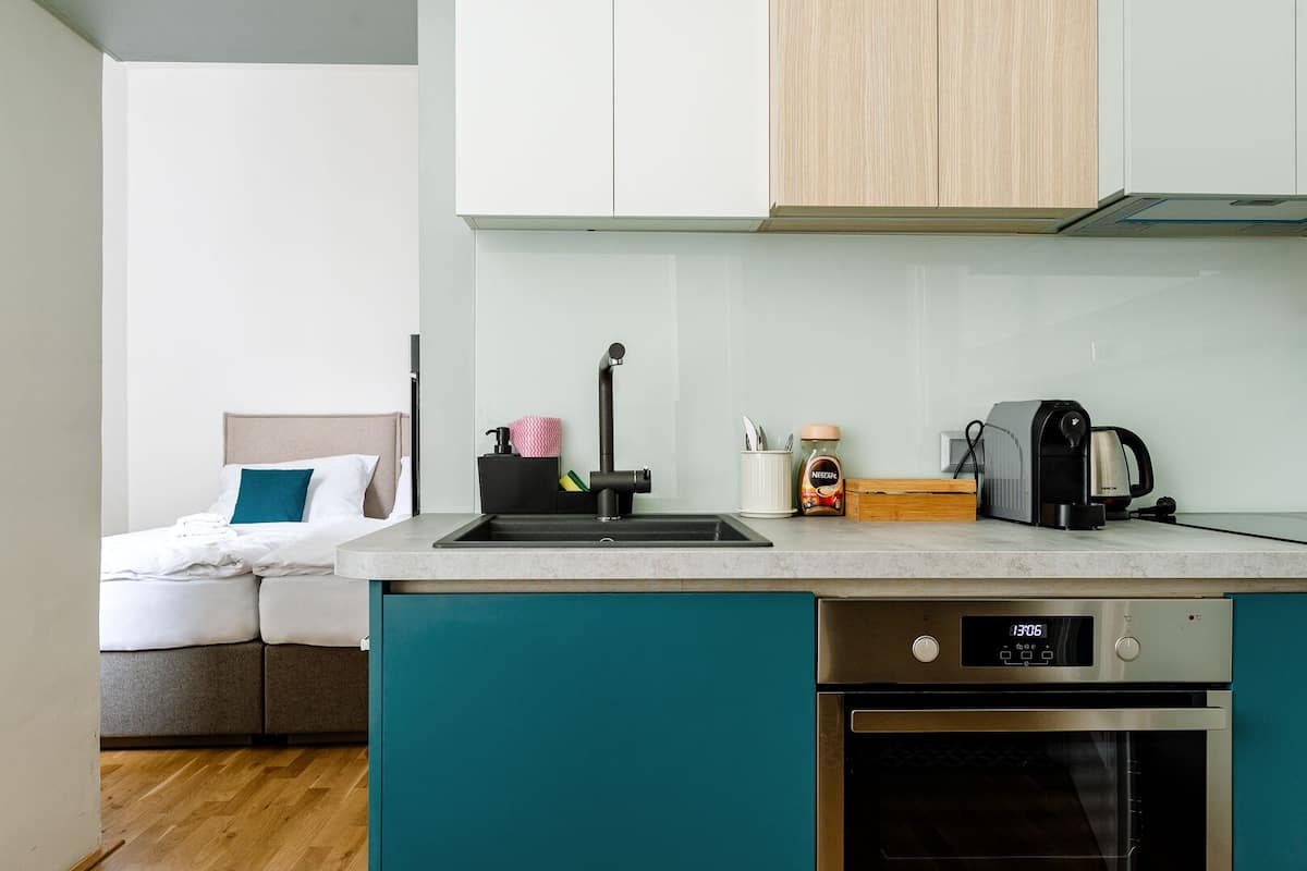 A compact kitchenette with a sink, coffee maker, and a clock displaying 13:06.