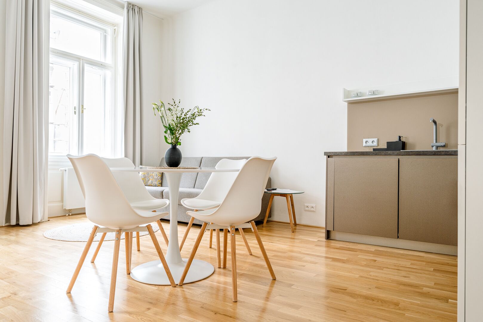 A modern dining area with a round table, white chairs, and a vase with flowers.