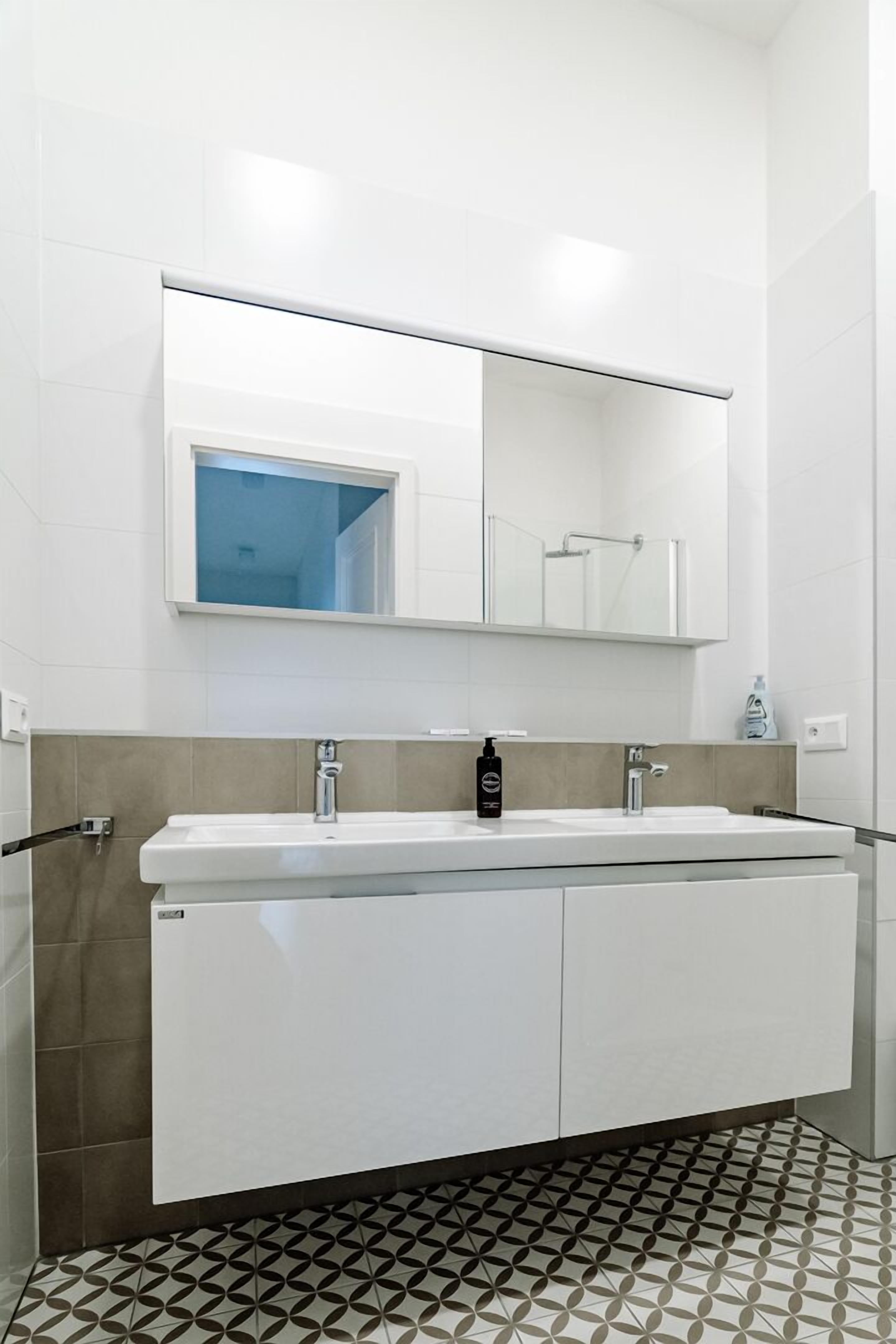 A modern bathroom with a double sink, a large mirror, and a patterned floor.