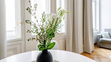 Une table blanche sur laquelle est posé un vase noir contenant des fleurs blanches et des feuilles vertes.