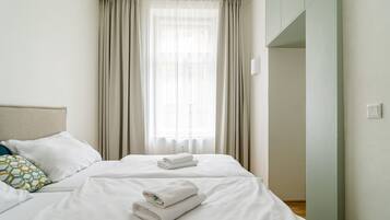 A hotel room with a bed, two pillows, a window with curtains, and a light switch on the wall.