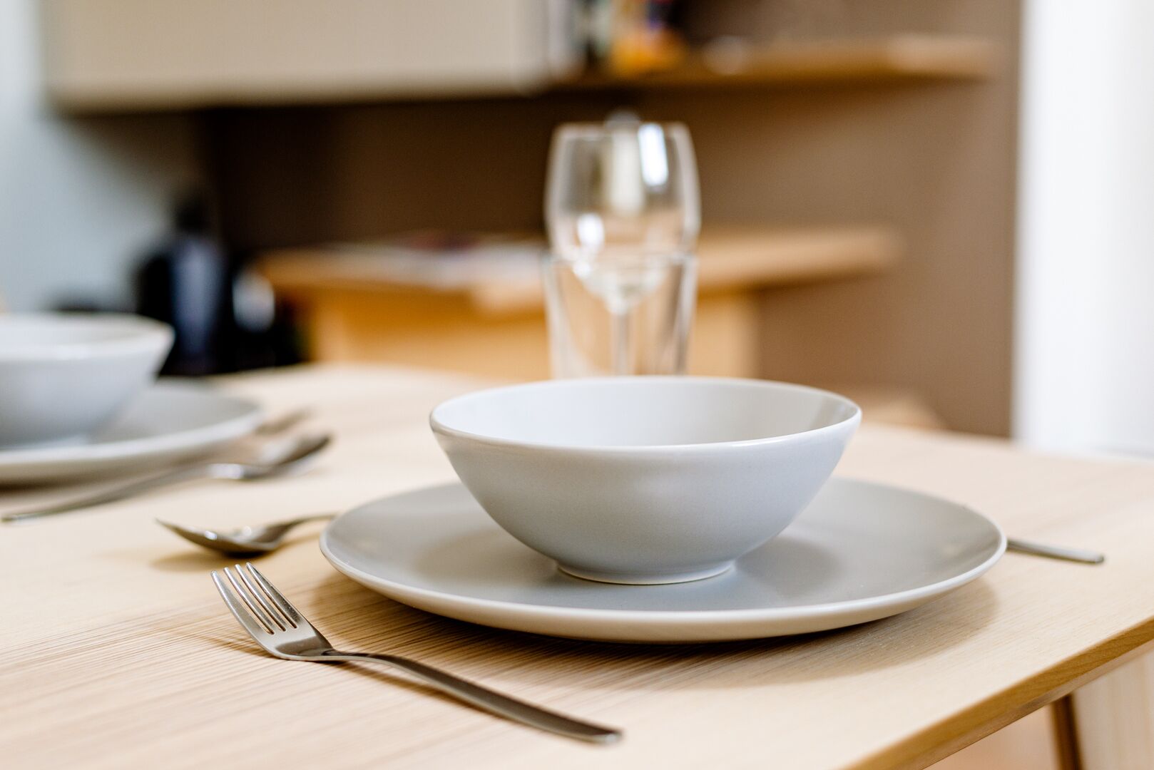 A dining table with a white bowl on a plate, a fork, and a glass of water.