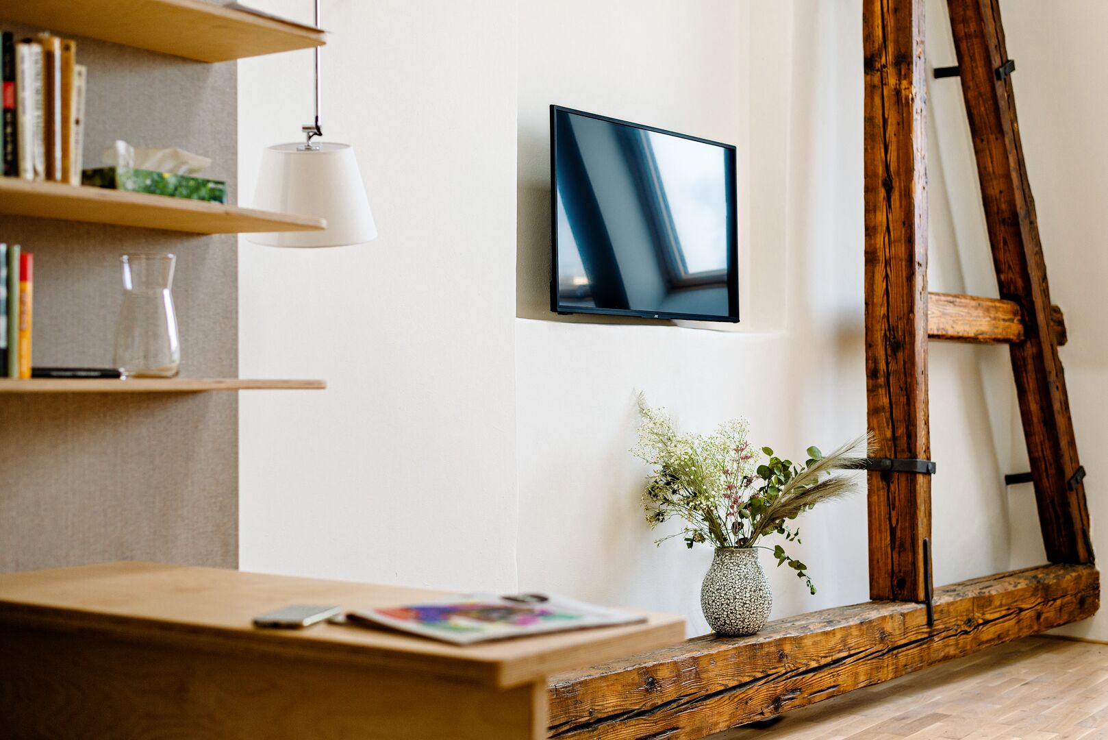 Un saló modern amb escriptori de fusta, televisió penjada, prestatges i una gerra decorativa.