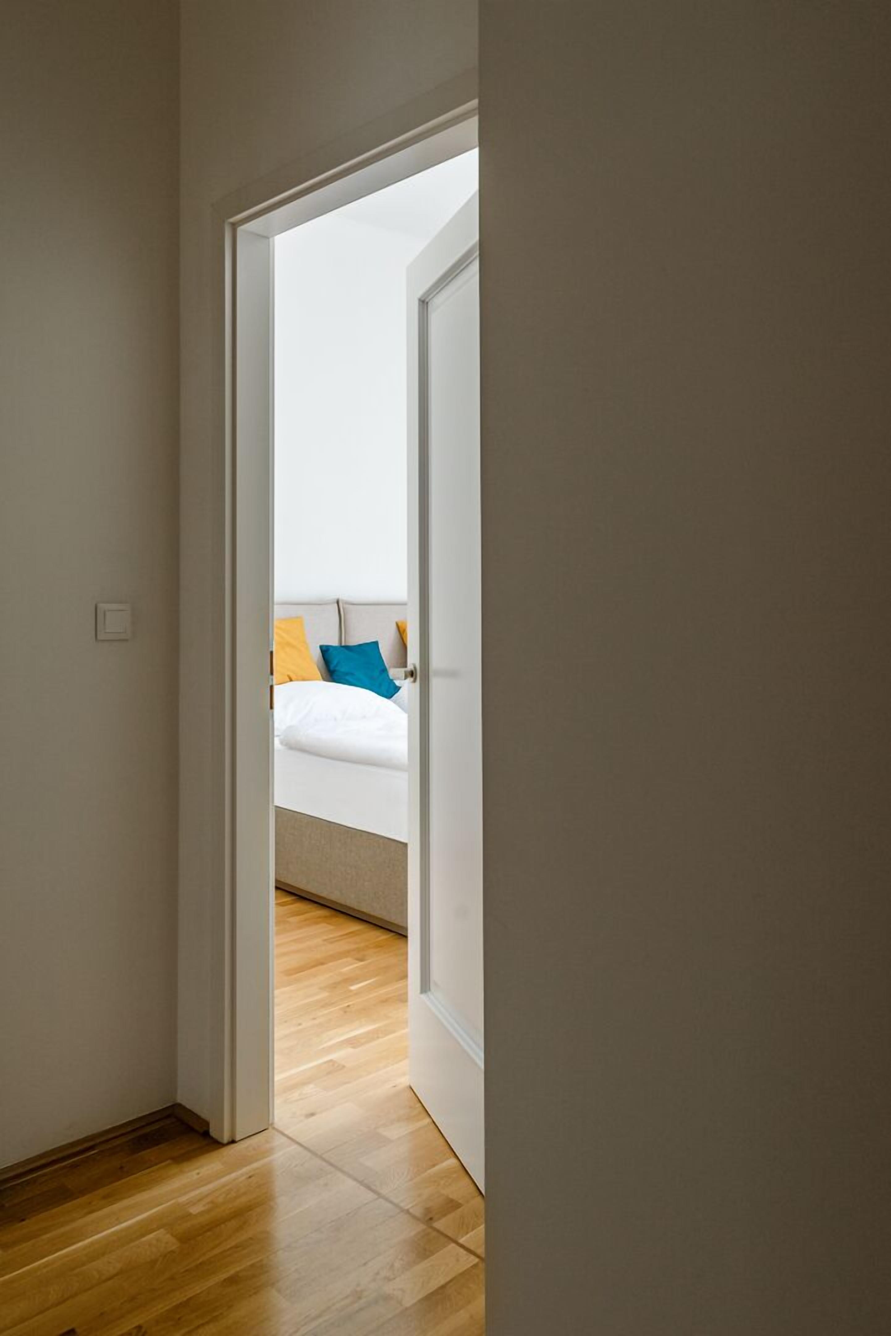 A narrow hallway leading to a bedroom with a bed and pillows.