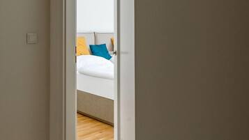 A narrow hallway leading to a bedroom with a bed and pillows.
