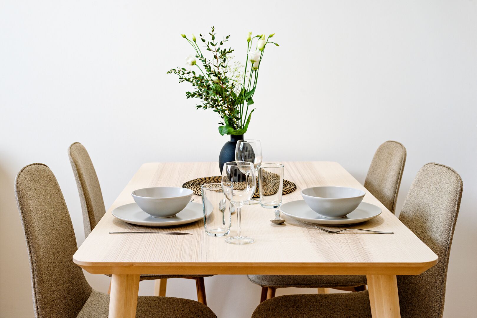 A dining table with two bowls, two glasses, and a vase with flowers.