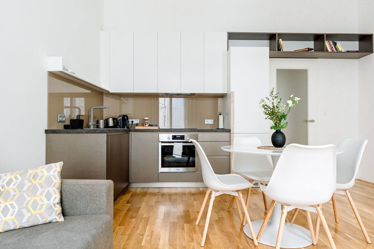 A modern kitchen with white cabinets, a built-in oven, and a dining area with white chairs and a table.