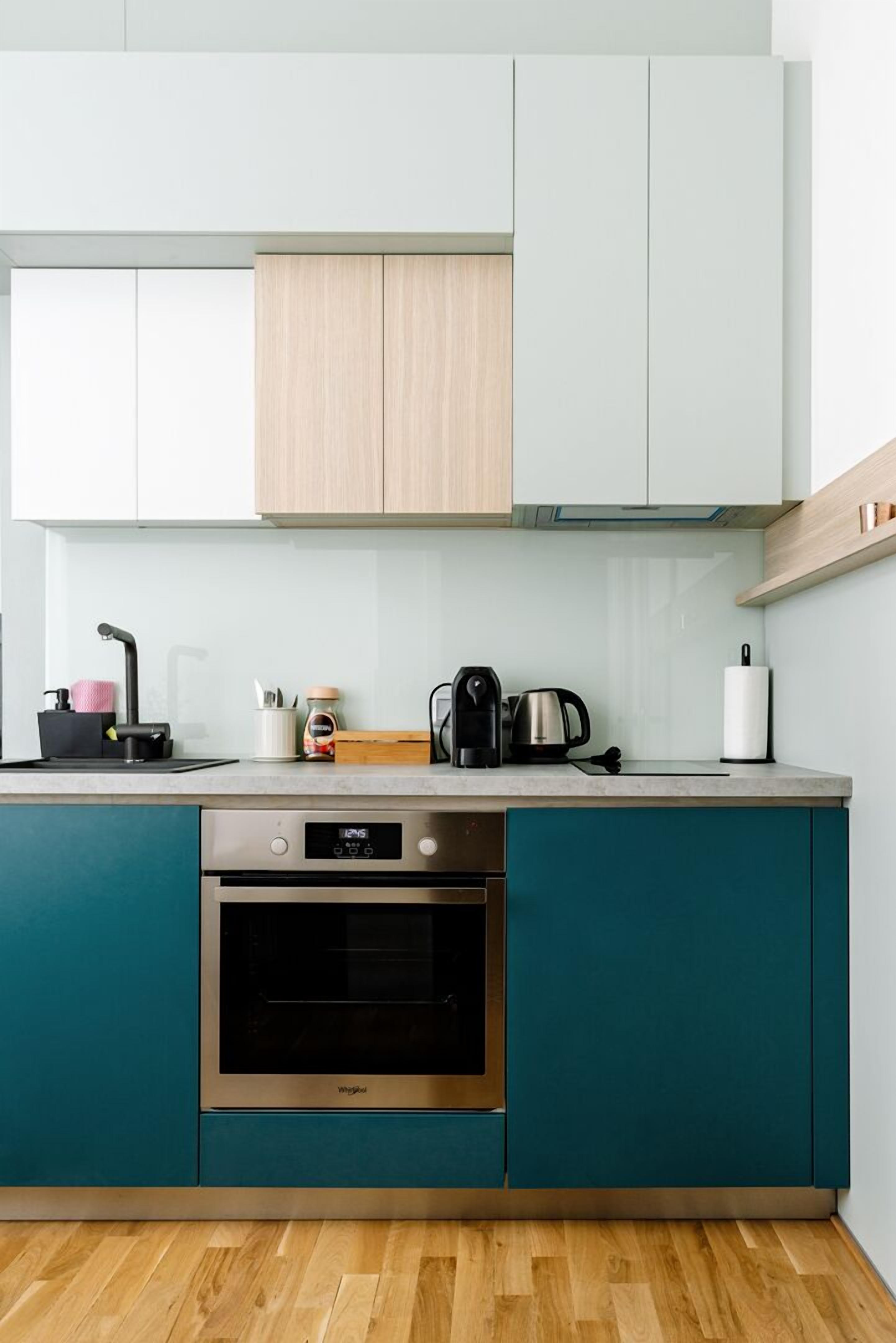 Eine moderne Küche mit türkis-blauen Schränken, einem Edelstahlbackofen und einer Kaffeemaschine auf der Arbeitsfläche.