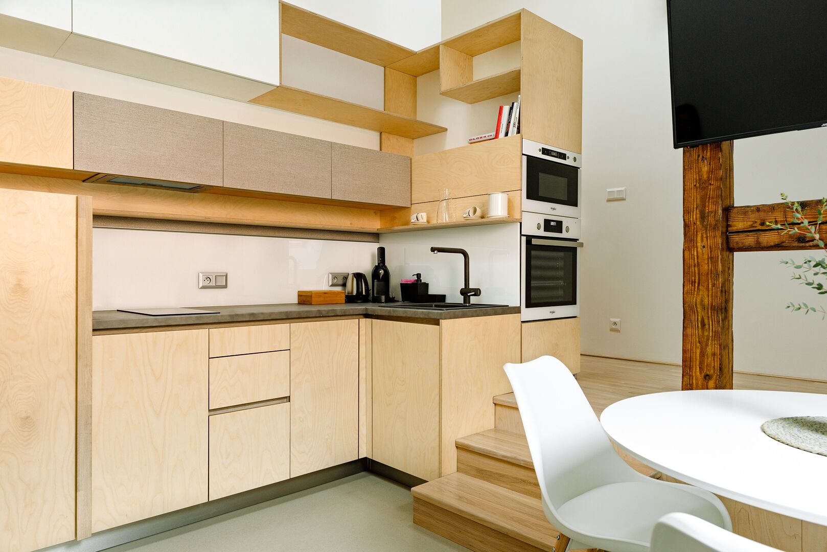 Une cuisine moderne avec des meubles en bois, un four encastré et un coin repas avec des chaises blanches.