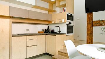 Une cuisine moderne avec des meubles en bois, un four encastré et un coin repas avec des chaises blanches.