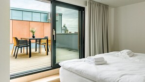 A hotel room with a bed, a balcony with a table and chairs, and a view of the outside. - Apartment BRNO (Brno)