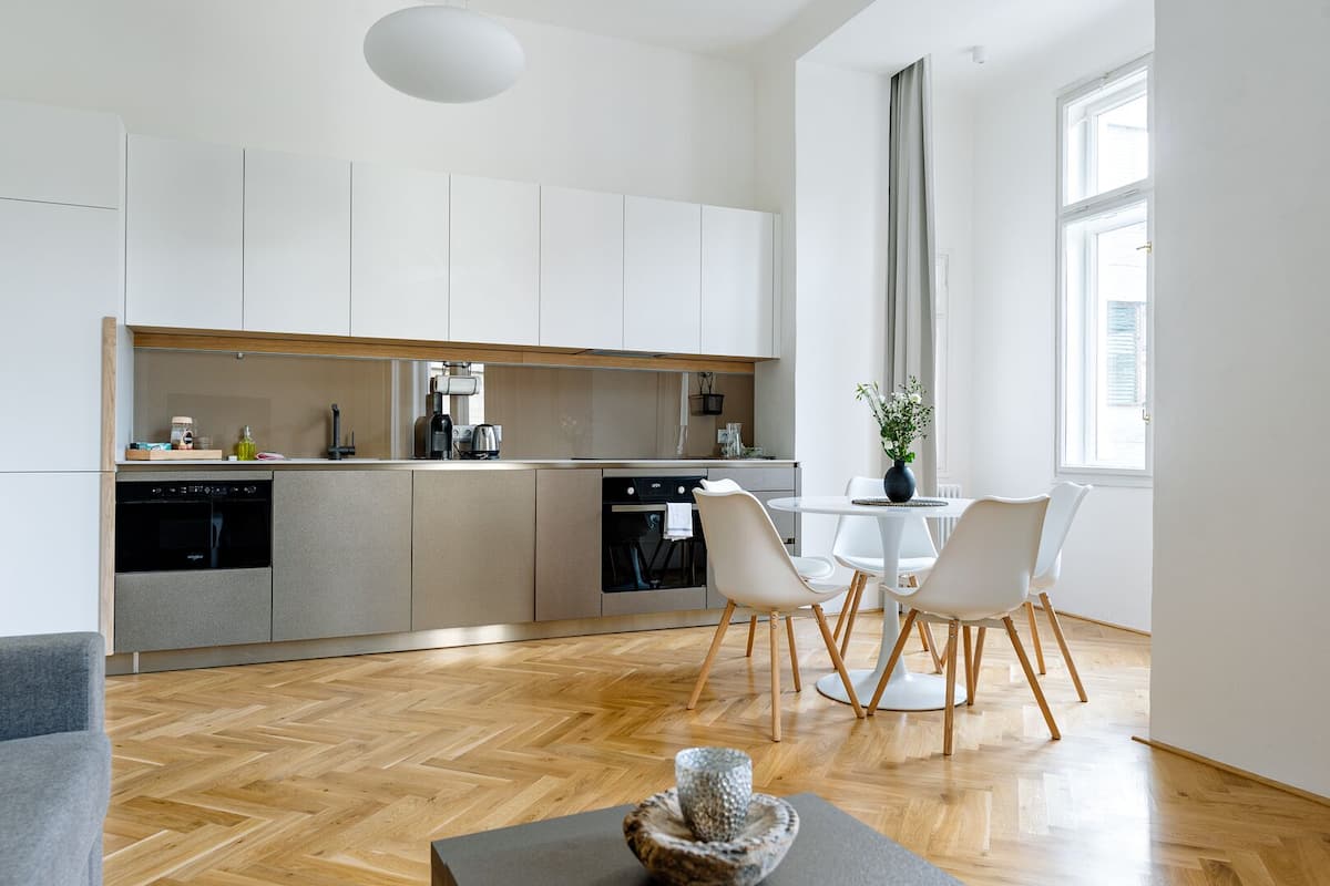 A modern kitchen with white cabinets, a dining area with a white table and chairs, and a large window providing natural light.
