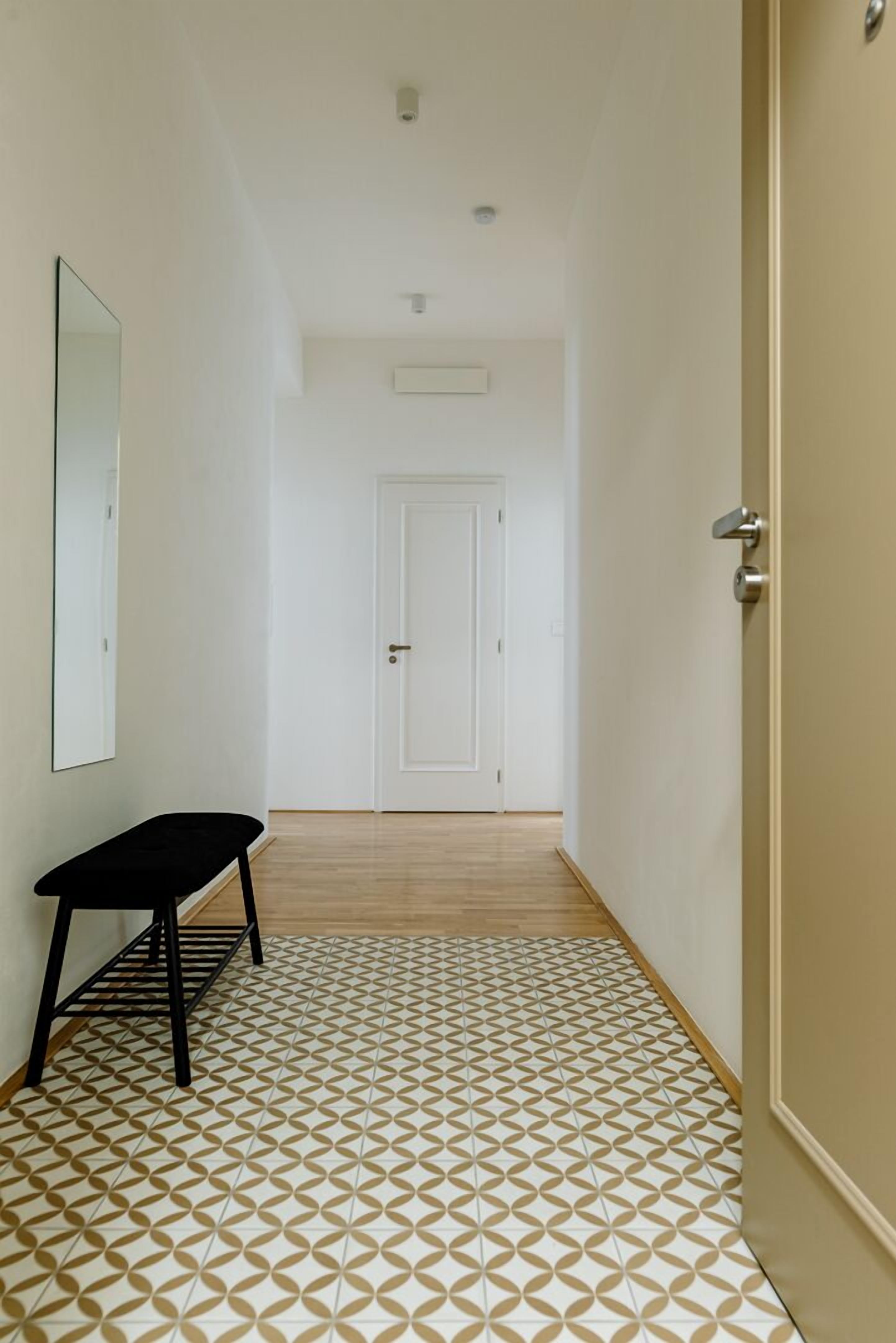 Un couloir avec un sol à motifs, un banc et une porte au fond.