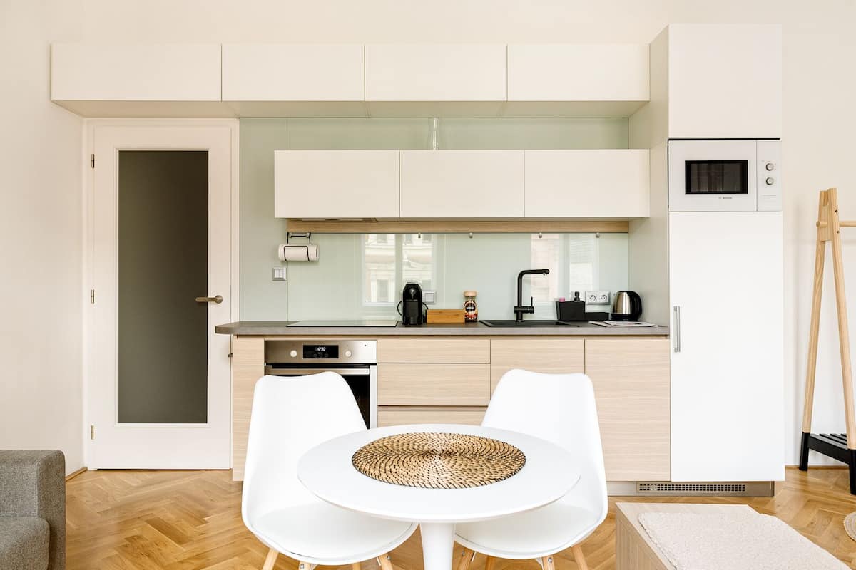 A modern kitchen with white cabinetry, a Bosch microwave, and a dishwasher. There is a dining area with a white table and chairs.