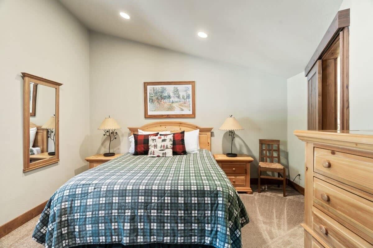 Un dormitorio con una cama, dos mesitas de noche, un aparador, una silla, un espejo y un cuadro en la pared.