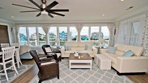 A spacious living room with a large window, a ceiling fan, and a view of the ocean. - Emerald Isle Lookout, Oceanview House in Emerald Isle, NC! (Emerald Isle)