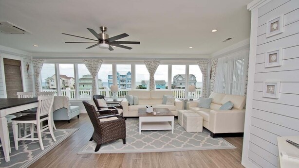A spacious living room with a dining area, a ceiling fan, and large windows offering a view of the sea. - Emerald Isle Lookout, Oceanview House in Emerald Isle, NC! (Emerald Isle)