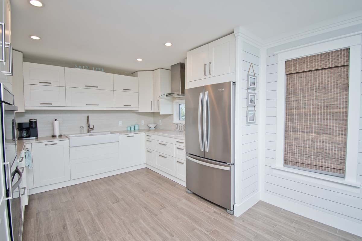A modern kitchen with white cabinetry, a stainless steel refrigerator, and a window with a bamboo blind.
